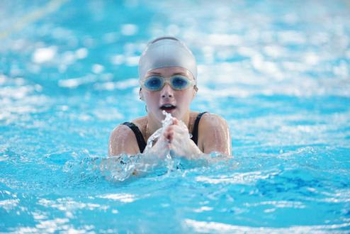 Junge Schwimmerin mit Badekappe und Schwimmbrille, die durch das Wasser paddelt. Blasen spritzen um sie herum.