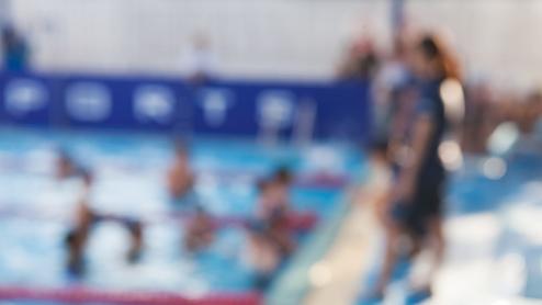 Unschärfe eines Schwimmbeckens mit Personen im Wasser und am Beckenrand, lebendige Farben und Aktivität sichtbar.