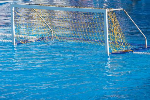 Wasserballtor mit gelbem Netz in einem blauen Schwimmbecken, teilweise im Wasser stehend.
